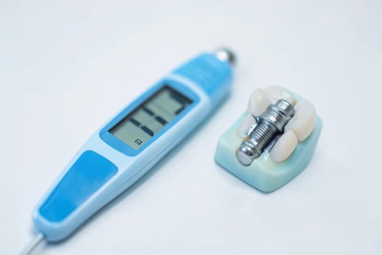 Close-up de um termômetro digital mostrando temperatura normal, ao lado de um modelo de implante dentário.