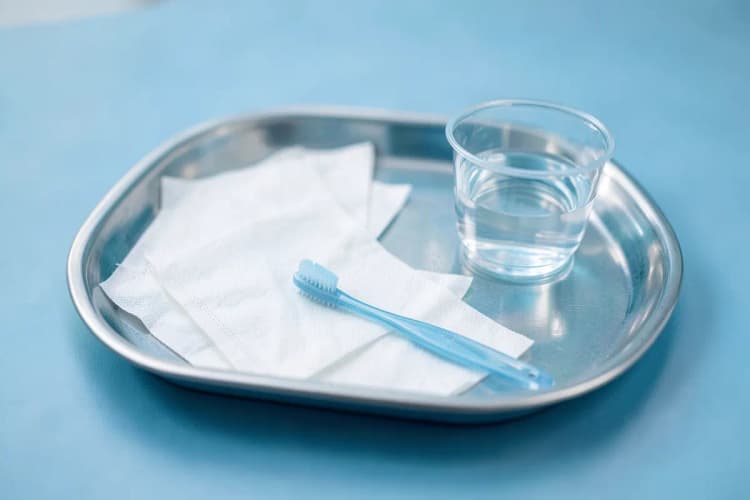 Bandeja com itens de cuidado pós-operatório: gaze, escova de dentes macia e copo com água.