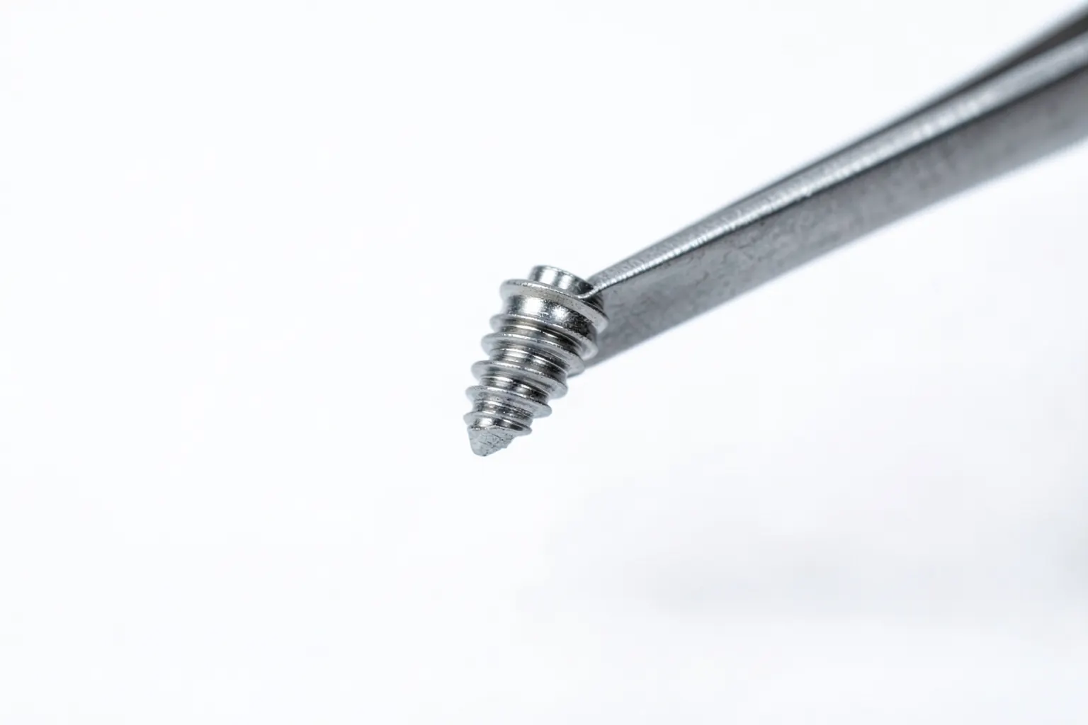 Close-up de um implante dentário de titânio sendo segurado por uma pinça cirúrgica sobre um fundo branco.