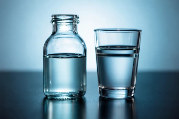 Frasco de antibiótico com um copo d'água ao lado.