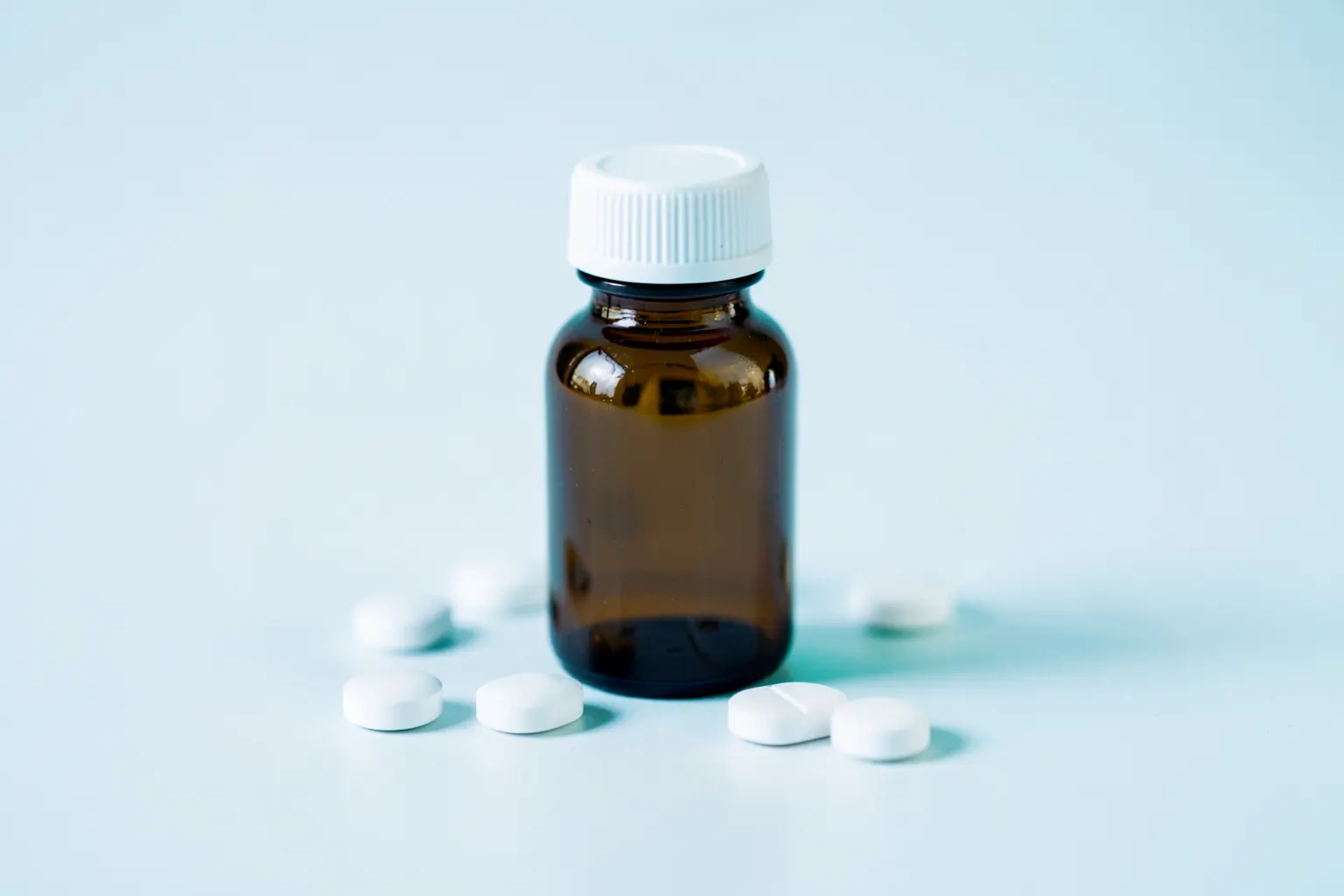 Frasco de antibiótico e comprimidos sobre uma superfície branca, com foco suave.